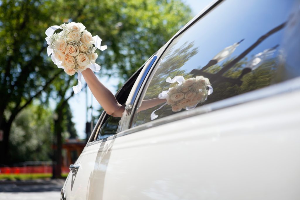 Bride waving hand from car holding flower bouquet